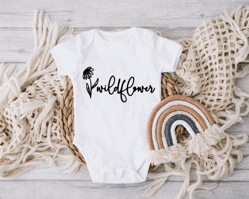 May include: White baby onesie with a black daisy and the text "wildflower" printed on the front.