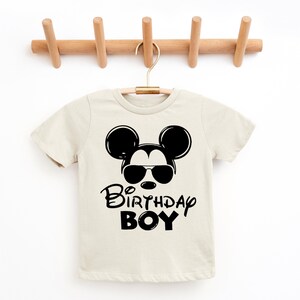 May include: A beige short-sleeved t-shirt with a black Mickey Mouse graphic wearing sunglasses and the text "Birthday Boy".