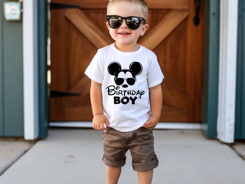 May include: A white t-shirt with a black Mickey Mouse graphic wearing sunglasses and the text "Birthday Boy".
