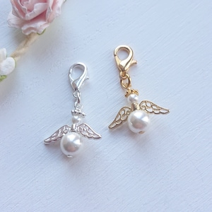 Può includere: Due ciondoli a forma di angelo in argento e oro con dettagli in perla. I ciondoli hanno un moschettone per essere attaccati a una borsa o ad un altro oggetto.