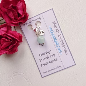 Op de afbeelding: Een zilveren bedel met een lichtblauwe aquamarijn-steen, een zilveren letter "I"-bedel en een zilveren kreeftclip. De bedel bevindt zich op een witte kaart met de tekst "March Birthstone ~AQUAMARINE~ Courage Friendship Awareness CherrycharmJewellery"