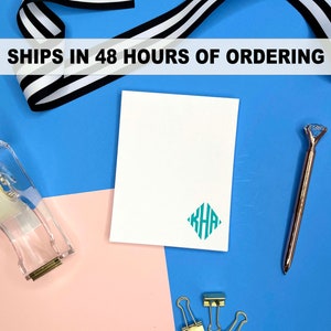 May include: A white card with a teal monogram in a diamond shape. The monogram reads "KHA". The card is on a blue surface with a pink surface to the left. There are gold paper clips and a gold pen on the blue surface. The text "SHIPS IN 48 HOURS OF ORDERING" is at the top of the image.