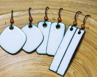 May include: A collection of white enamel earrings with dark teal edges and copper-toned beads on dark metal hooks. The set includes diamond-shaped, rectangular, and long bar-shaped pendants labeled with the letters I, G, and H respectively.