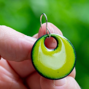 May include: A circular earring featuring a glossy, vibrant lime green center that transitions into a dark, forest green border. The piece has a central circular cutout and is suspended from a simple, thin silver-toned metal hook wire.