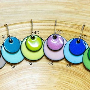 May include: Eight pairs of earrings with two layered circles. The top circle is a solid colour and the bottom circle is a lighter shade of the same colour. The colours are brown, blue, green, yellow, pink, and light blue.