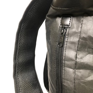 May include: A black backpack with a zippered pocket and a mesh padded strap. The backpack is made of a water-resistant material.