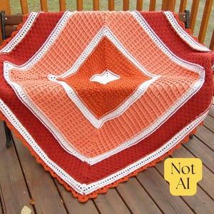 May include: A square crochet blanket featuring a diamond pattern in shades of dark red, orange, and peach, accented with white borders. The blanket has a textured waffle-like stitch throughout and a scalloped edge, with a small white heart shape.