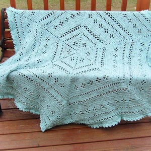 May include: A light blue crocheted throw blanket with a delicate floral pattern. The blanket is draped over a wooden bench.