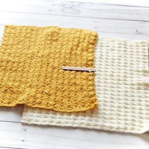 May include: Two crocheted blankets, one yellow and one white, with a textured waffle stitch pattern. The blankets are laid out on a white wooden surface. The text "oceanmintdesigns" is visible on a wooden tag.