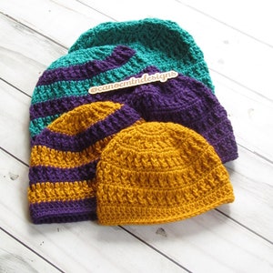 May include: Three crocheted hats in different colours and patterns. The hats are stacked on top of each other. The top hat is teal, the middle hat is purple and teal stripes, and the bottom hat is mustard yellow. The hats are on a white wooden surface. The text '@canoemntdesigns' is on a small wooden tag.