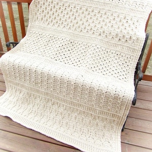 May include: A crocheted throw blanket in a cream color with a lacy pattern. The blanket is folded and draped over a wooden bench.
