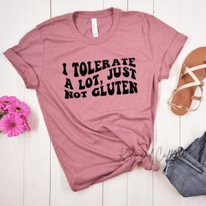 May include: A mauve t-shirt with the text "I tolerate a lot, just not gluten" in black, retro-style font.