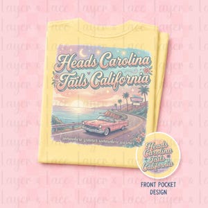 May include: A pale yellow t-shirt featuring a graphic print of a pink vintage convertible driving along a coastal road at sunset. The text reads Heads Carolina Tails California and somewhere greener somewhere warmer with a small motel sign.