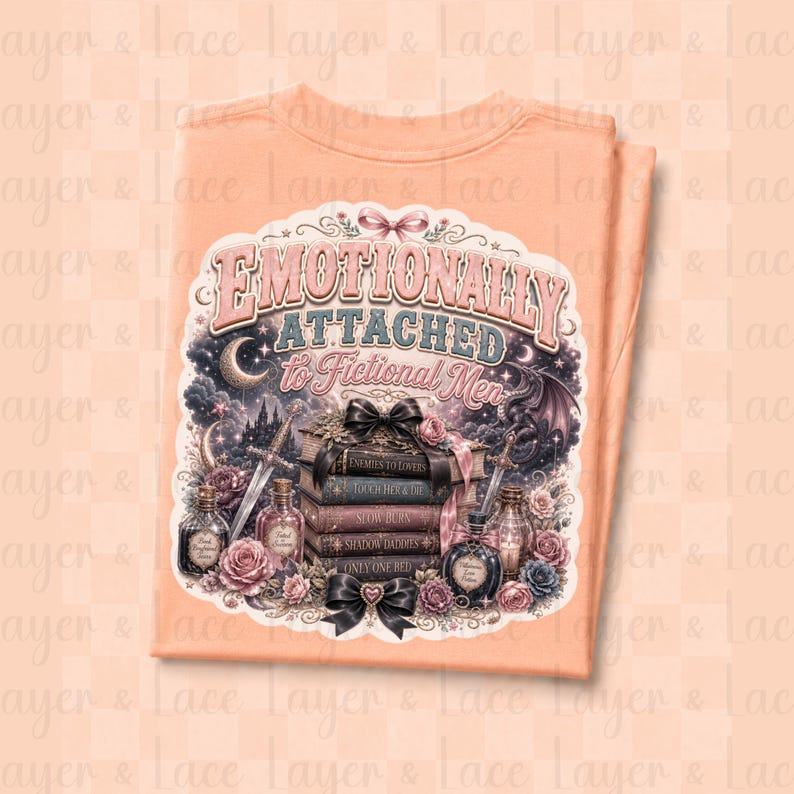 May include: Peach-colored t-shirt featuring a graphic design with the text "Emotionally Attached to Fictional Men." The design includes a stack of books, roses, potion bottles, a castle, and a dragon. The design is in shades of pink, blue, and black.