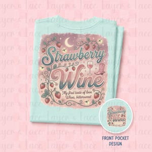 May include: A light mint green t-shirt featuring a graphic print with the text Strawberry Wine My first taste of love Whoa, bittersweet. The design includes illustrations of strawberries, vines, a wine glass, a crescent moon, and a cowboy boot.