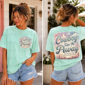 May include: A light mint green t-shirt featuring a small graphic on the front left chest and a large graphic on the back. Both graphics display the text "Cowboy Take Me Away" with a desert landscape, cacti, and a crescent moon in pastel colors.