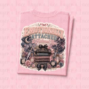 May include: A light pink t-shirt featuring a graphic design with the text "Emotionally Attached to Fictional Men." The design includes a stack of books, swords, roses, and potion bottles, with a fantasy theme.