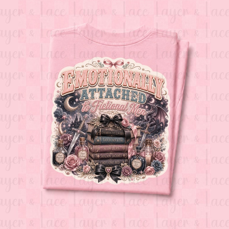 May include: A light pink t-shirt featuring a graphic design with the text "Emotionally Attached to Fictional Men." The design includes a stack of books, swords, roses, and potion bottles, with a fantasy theme.