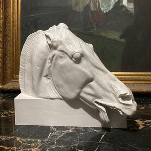 May include: White ceramic sculpture of a horse's head with its tongue sticking out. The sculpture is on a white base and is sitting on a black marble surface.