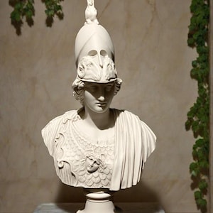 May include: White marble bust of a woman wearing a helmet with ram horns and a decorative breastplate. The bust is on a white marble base.