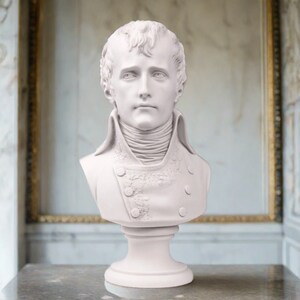 May include: White plaster bust sculpture of a man with short hair and a high collar. The bust is on a white pedestal.