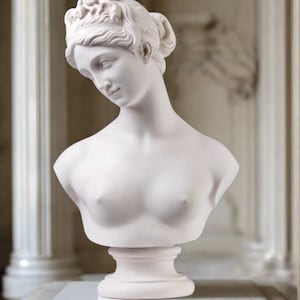 May include: White plaster bust sculpture of a woman with a detailed hairstyle. The bust is on a white pedestal.