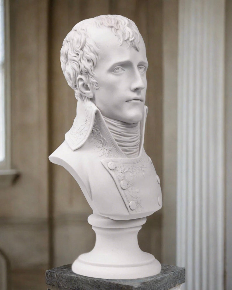 May include: White plaster bust sculpture of a man with short hair, wearing a high-collared jacket with decorative details. The bust is mounted on a white pedestal.