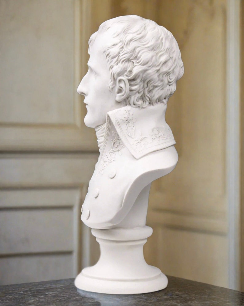 May include: White plaster bust sculpture of a man with short, wavy hair. The bust is on a white pedestal.