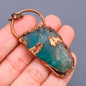 Op de afbeelding: Een hanger van koperdraad met een groene agaat-steen met gouden accenten. De hanger heeft een lus aan de bovenkant om aan een ketting te bevestigen.