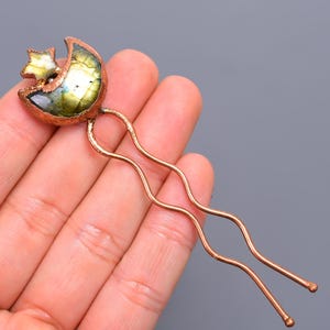 Puede incluir: Una horquilla de pelo de cobre con un diseño de media luna y estrella. La luna está hecha de labradorita iridiscente verde y dorada.