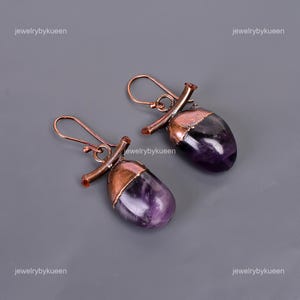 May include: A pair of amethyst gemstone earrings with copper wire accents. The earrings are shaped like a teardrop and have a copper wire wrapped around the top of the stone.