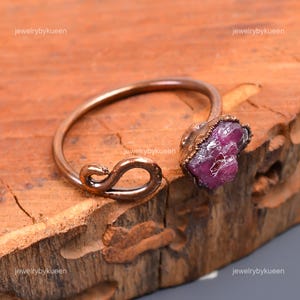 May include: A copper wire bracelet with a large, raw pink ruby gemstone. The bracelet is open and has a unique, twisted design.