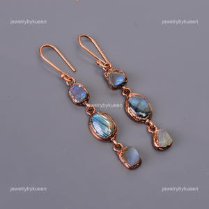 May include: A pair of long, copper dangle earrings with multiple iridescent blue labradorite stones. The stones are set in copper wire and have a natural, irregular shape.