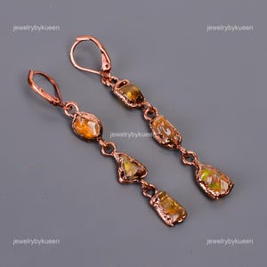 May include: A pair of copper earrings with a dangling design. Each earring features four teardrop-shaped stones with a golden iridescent sheen.