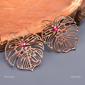 May include: A pair of copper earrings shaped like a leaf with a pink gemstone in the center of each leaf.