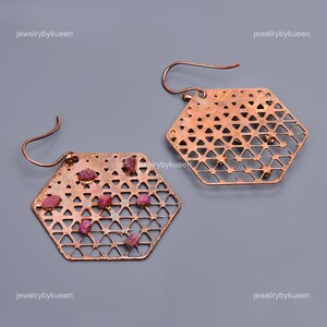 Può includere: Un paio di orecchini in rame con un design esagonale geometrico. Gli orecchini sono adornati con piccole pietre di rubino rosso.