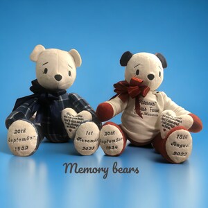 May include: Two white plush teddy bears with embroidered details. One bear is wearing a blue plaid shirt and the other is wearing a white shirt with red trim. Both bears have hearts on their paws with dates embroidered on them. The bears are sitting on a blue surface. The text "Memory bears" is written below the bears.