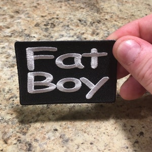 May include: Black fabric patch with white embroidered text that reads "Fat Boy".