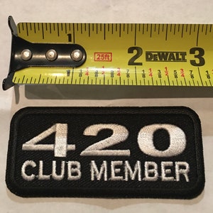 May include: Black rectangular patch with white embroidered text reading "420 CLUB MEMBER." A yellow tape measure is above the patch, showing measurements in inches.