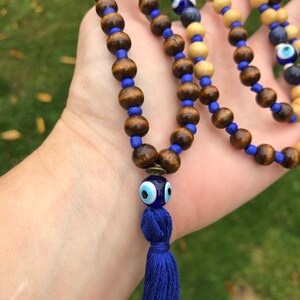 May include: A beaded necklace with dark brown wooden beads, blue glass beads, and a blue tassel. The necklace includes a decorative blue glass bead with an eye design.