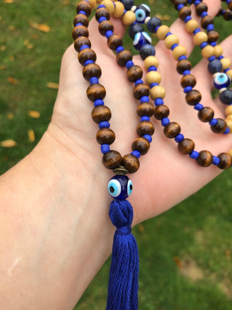 May include: A beaded necklace with dark brown wooden beads, blue glass beads, and a blue tassel. The necklace includes a decorative blue glass bead with an eye design.