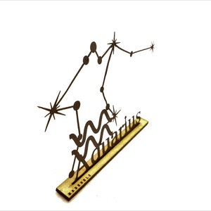 May include: A wooden cutout of the Aquarius constellation with the word "Aquarius" written below it. The cutout is on a wooden base with the word "MADEBOULC" written on it.