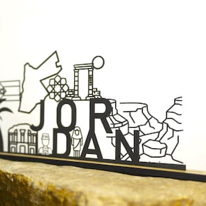 Puede incluir: Letrero de madera cortado con láser en blanco y negro con la palabra "JORDAN" y monumentos emblemáticos. El letrero está montado sobre una base de madera y sobre un fondo neutro.