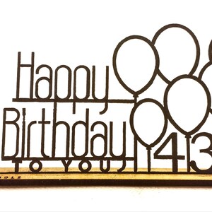 Puede incluir: Un letrero de metal negro de Feliz Cumpleaños para ti con globos y el número 43. El letrero está sobre una base de madera.
