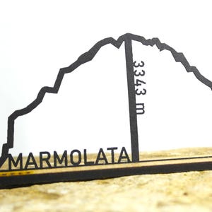 May include: Black laser-cut wooden Marmolada mountain range silhouette with the height of 3343 m. The mountain name is displayed at the base. The silhouette is mounted on a wooden base.