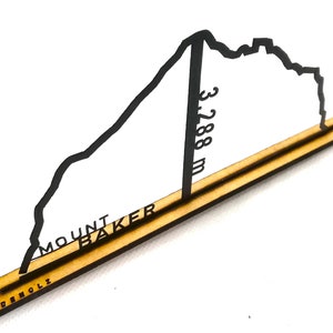 Peut inclure: Découpe en bois du Mont Baker, avec l'inscription "MOUNT BAKER" et "3 288 m". Le contour de la montagne est noir, sur une base marron clair. La marque "MADENHOLZ" est également visible.