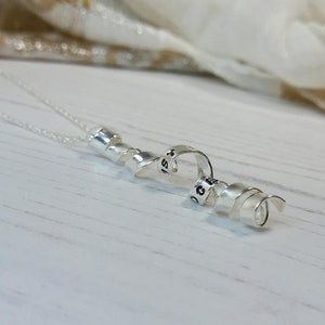 May include: Silver necklace with a heart charm and a spiral design. The heart charm has the word "love" engraved on it.