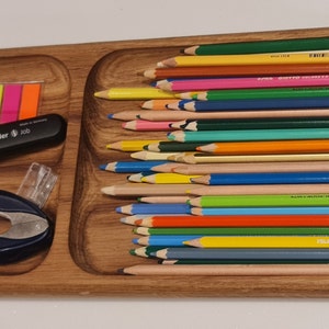 May include: A wooden tray with four compartments, containing colored pencils, highlighters, a pencil sharpener, and a small package of candy. The tray is made of light brown wood and has a smooth finish.