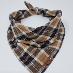 May include: A brown, tan, and black plaid bandana with a leather patch that says "Pawsitive Vibes" in black lettering. The bandana is tied in a knot at the top.