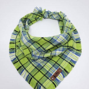 May include: Green, blue, and white plaid dog bandana with frayed edges and a brown leather patch with the text "The Pawsitive" in white.